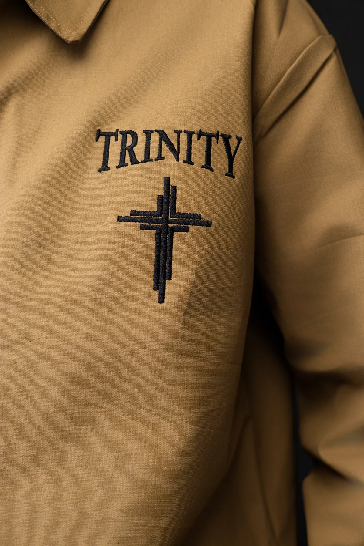 Close view of the Trinity name and logo embroidered on the tan jacket